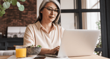 A woman sits at a computer in a cozy home environment, reviewing her peer-to-peer investments.