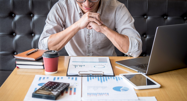 Accredited investor reviewing investment options with printouts, laptop, calculator, and coffee. 