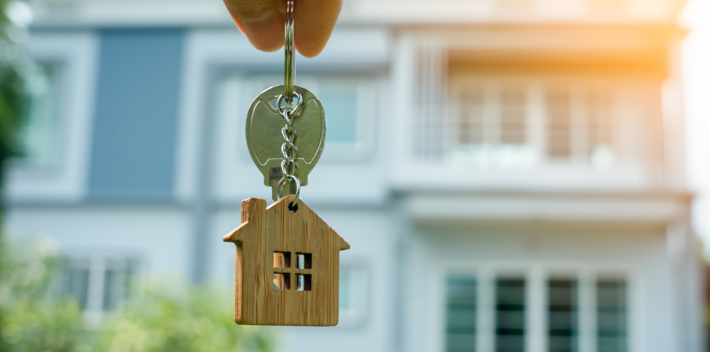 Key chain with a single key and small wooden house decorative element in front of rental properties. 